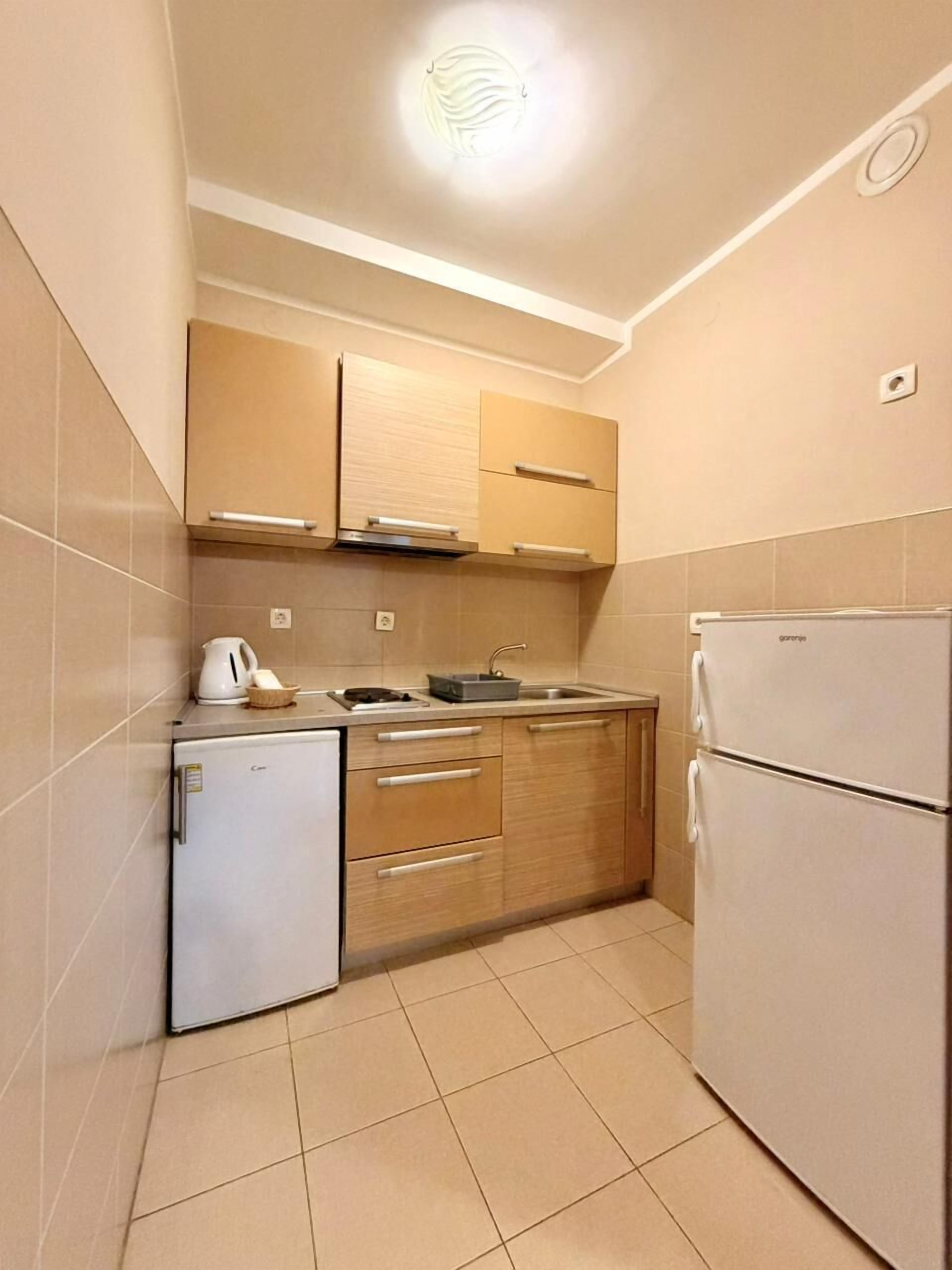 A compact kitchen with a refrigerator, stove, sink, and wooden cabinets.