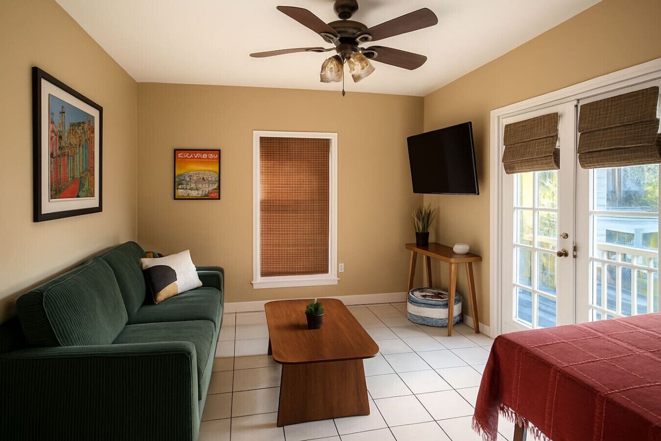 Ein Wohnzimmer mit einem grünen Sofa, einem Holztisch, einem Deckenventilator, einem Fernseher und einer Tür mit Fenster.