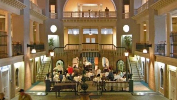 Ein mehrgeschossiges Atrium mit einer zentralen Treppe, mehreren Balkonen und einem Essbereich mit Tischen und Stühlen.