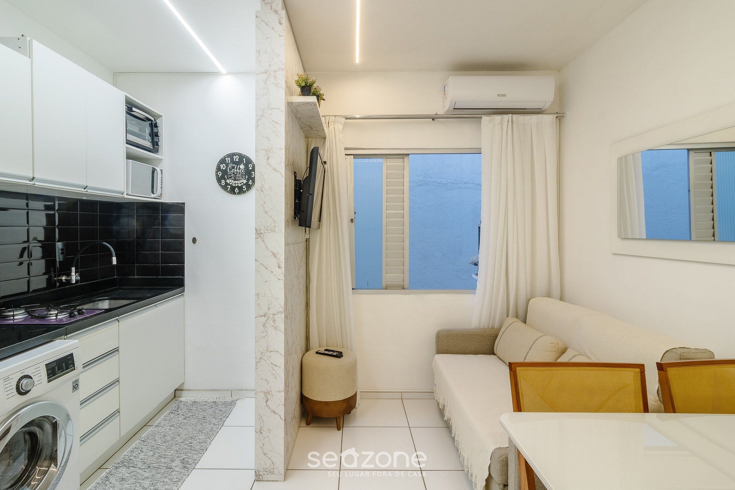 A compact living space with a kitchenette, a sofa, a dining table, and a view of the sea.