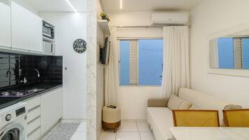 A compact living space with a kitchenette, a sofa, a dining table, and a view of the sea.