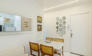 Un coin repas comprenant une table blanche, quatre chaises, un canapé, un réfrigérateur et une porte.