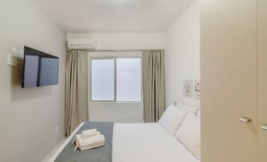 Une chambre d’hôtel équipée d’un lit, d’un téléviseur à écran plat fixé au mur, d’un système de climatisation, d’une fenêtre avec des rideaux et d’une armoire.