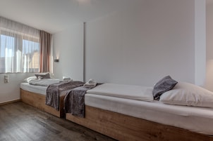 Ein modernes Schlafzimmer mit einem hölzernen Plattformbett, einem Nachttisch und einem Fenster mit transparenten Vorhängen.