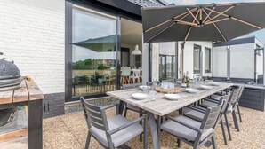 Ein Essbereich im Freien mit Holztisch und Stühlen, einem großen Sonnenschirm und einem Grill.