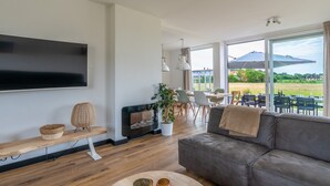 Ein modernes Wohnzimmer mit Flachbildfernseher, Kamin, Sofa und Essbereich mit Gartenmöbeln.