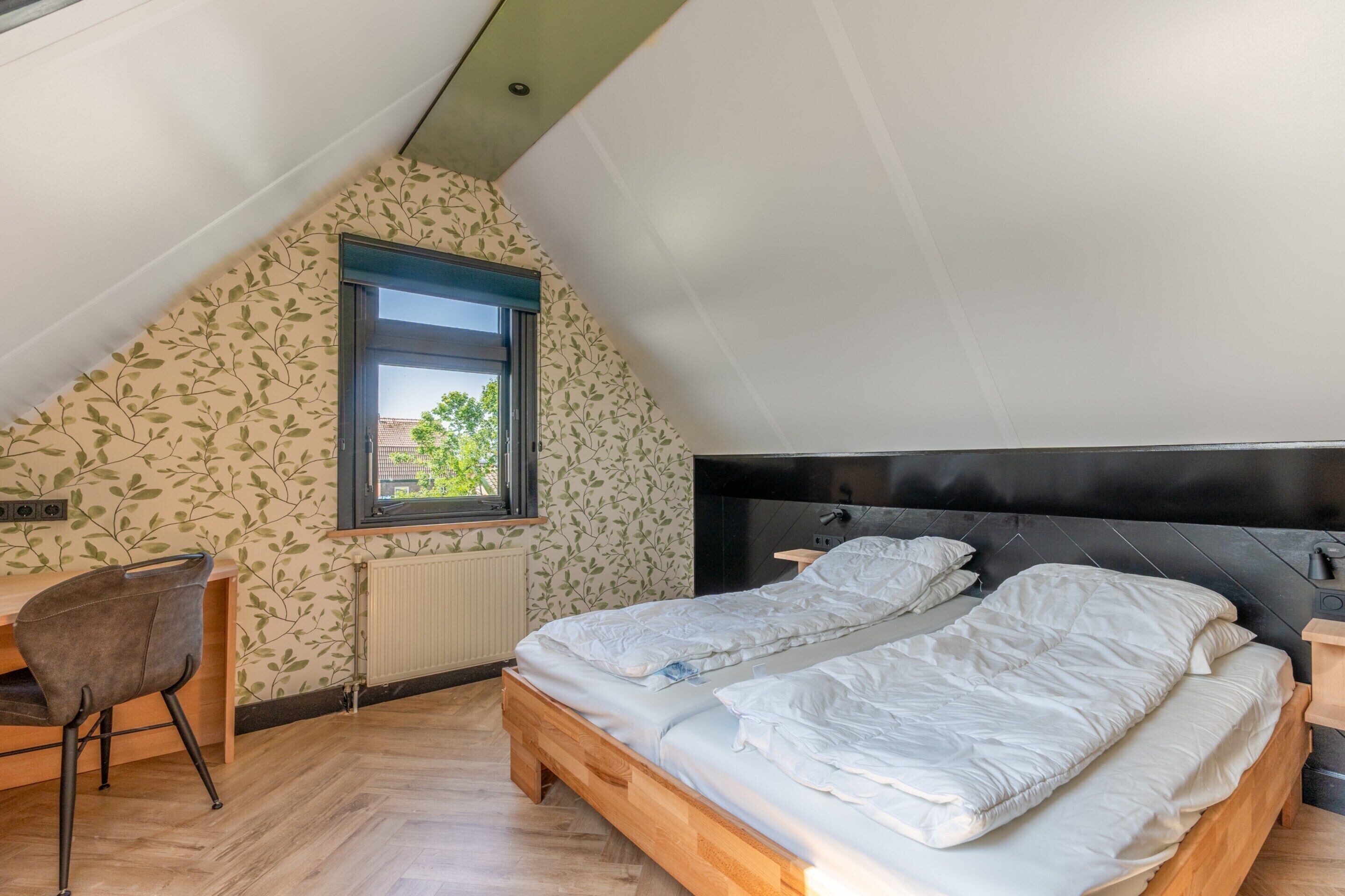 A bedroom with a sloped ceiling, a wooden bed, a desk, and a chair.