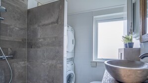 Et moderne badeværelse med en bruseniche i beton, en vaskemaskine og en stor håndvask.