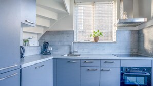 Et moderne køkken med lysegrå skabe, en stålvask, indbygget ovn og et vindue med persienner.