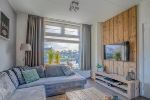 Una sala de estar moderna con un sofá gris, un mueble de televisión de madera y un ventanal con cortinas.