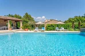 A swimming pool with lounge chairs and umbrellas, surrounded by greenery and a building with a tiled roof. - Country House "Le Cyprès" (Crillon-le-Brave)
