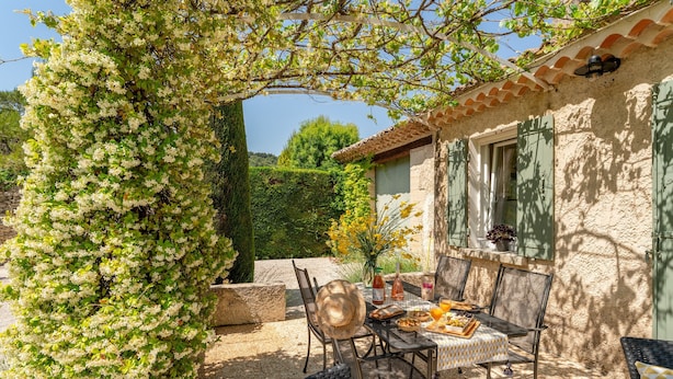 Eine Terrasse mit Esstisch, umgeben von Korbstühlen, unter einer Pergola mit rankenden Pflanzen.