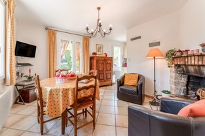 A dining area with a table, chairs, and a television. There is a fireplace with a mantel and a sofa in the living area.
