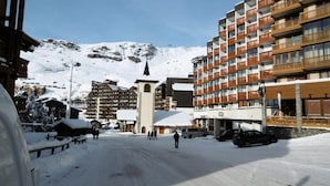 Een met sneeuw bedekte straat met gebouwen, waaronder een hotel met balkons en een kerk met een torenspits.