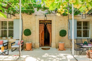 A stone building with a door, potted plants, outdoor seating, and a table.