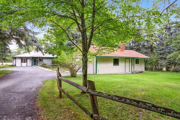 A rustic cabin with a red roof, surrounded by lush greenery and a wooden fence.