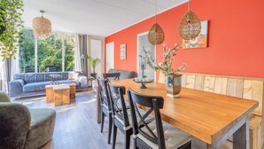 Una sala de estar moderna con una mesa de comedor de madera, sillas negras, un sofá azul y un ventanal con vistas a zonas verdes.