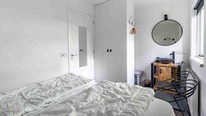 Una habitación minimalista con dos camas, un armario de madera, un espejo redondo y un radiador.