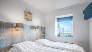 Un dormitorio con dos camas, cabecero de madera, lámparas fijadas a la pared, una ventana con vistas y un televisor montado.