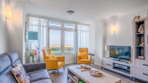 Una sala de estar moderna con un sofá, dos sillones, una mesa de centro, un televisor y un aparador con adornos.