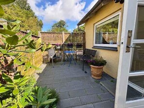 A patio area with a table and chairs, a wooden fence, and potted plants.