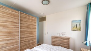 A bedroom with a bed, a wooden wardrobe, a dresser, and a painting on the wall. - 2 Person Island View Apartment (De Koog)