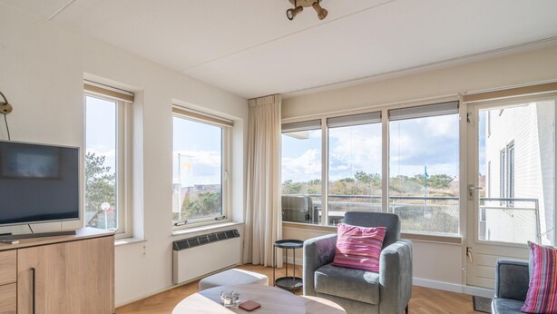 A spacious living room with a flat-screen TV, a round coffee table, and a grey sofa with a pink pillow. - 2 Person Island View Apartment (De Koog)
