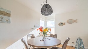 A round dining table with four chairs, a hanging light fixture, a vase with flowers, and a wall with a fish decoration and a sign. - 2 Person Island View Apartment (De Koog)