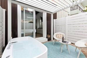 A modern outdoor bathroom with a large bathtub, a laptop on a small table, and a chair with cushions. - Borgo Centrale Rooms (Pescara)
