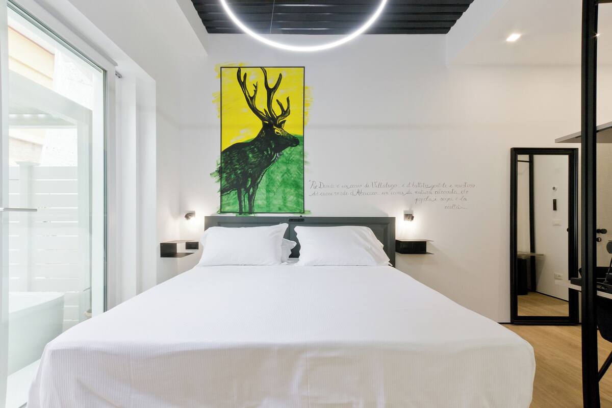 Ein modernes Hotelzimmer mit einem großen Bett, einem Wandbild von einem Hirsch und Blick durch eine Glastür nach draußen.