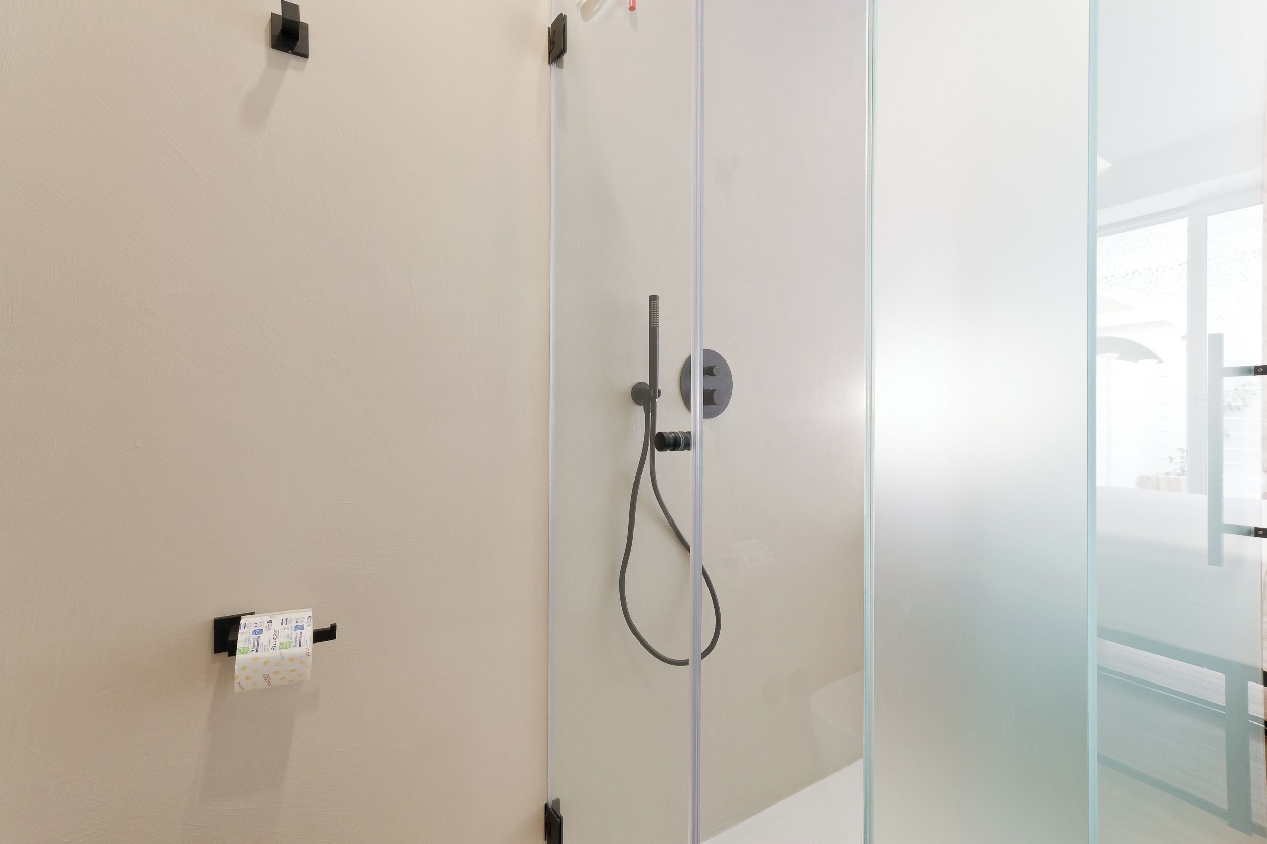A glass shower enclosure with a control panel and a handheld showerhead.