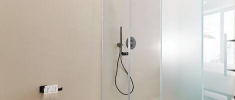 A glass shower enclosure with a control panel and a handheld showerhead.