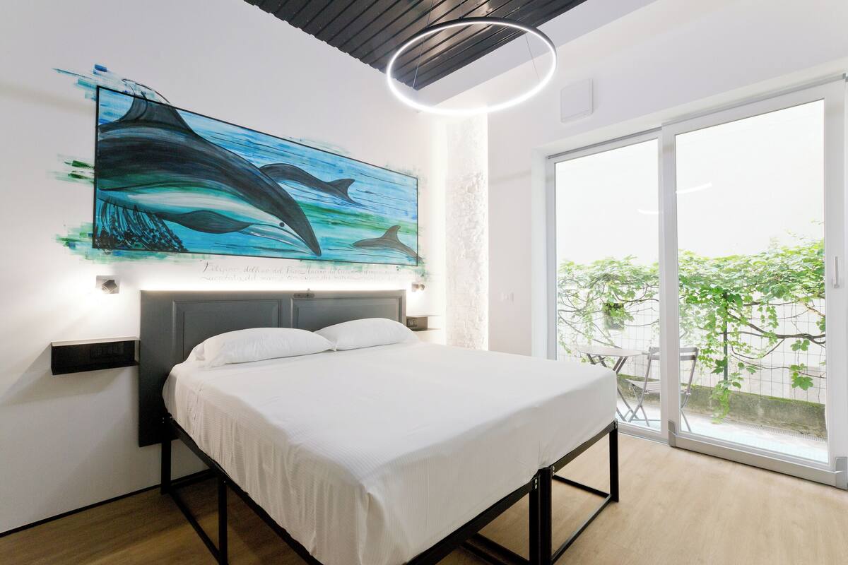 Ein modernes Schlafzimmer mit einem Bett, einem großen Fenster und Wandkunst mit Delphinen.