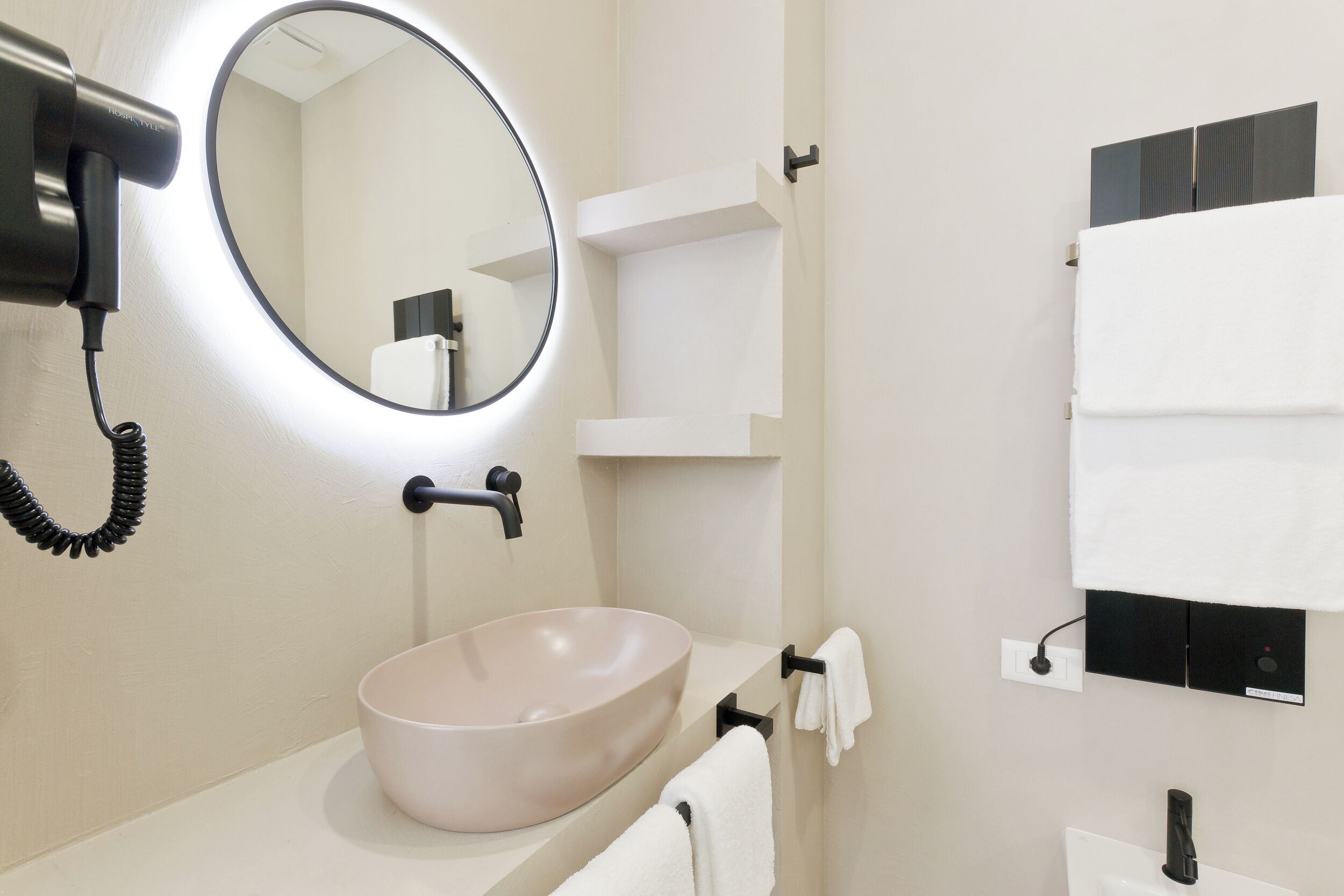 A modern bathroom with a round mirror, a beige sink, and a towel rack.