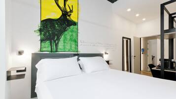 Una habitación de hotel con una cama, un cuadro de un ciervo, una mesita de noche, una lámpara de pared y una puerta que da a otra habitación.
