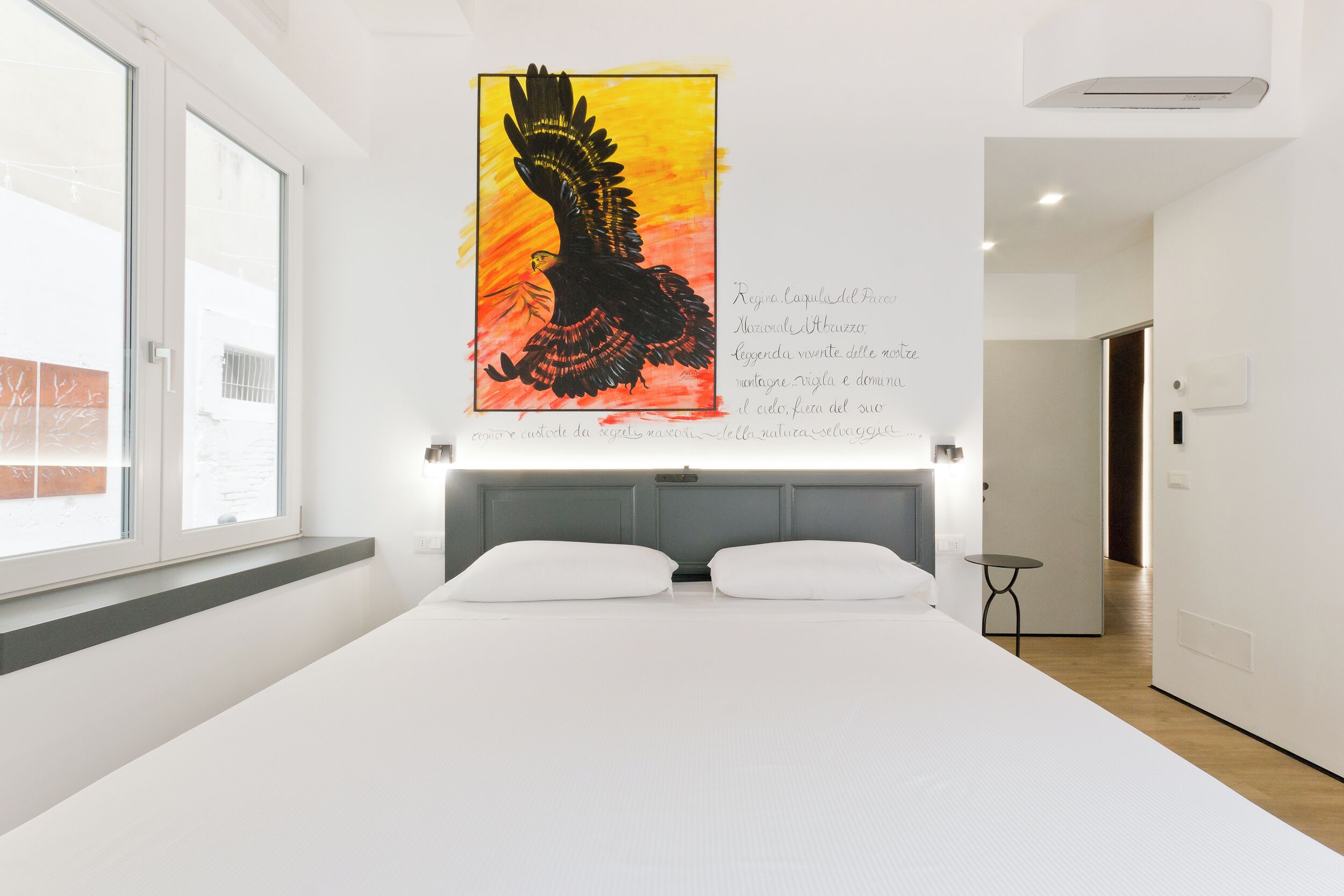 Una habitación de hotel moderna con una cama grande, un ventanal con vistas y una obra de arte de un águila colgada en la pared.