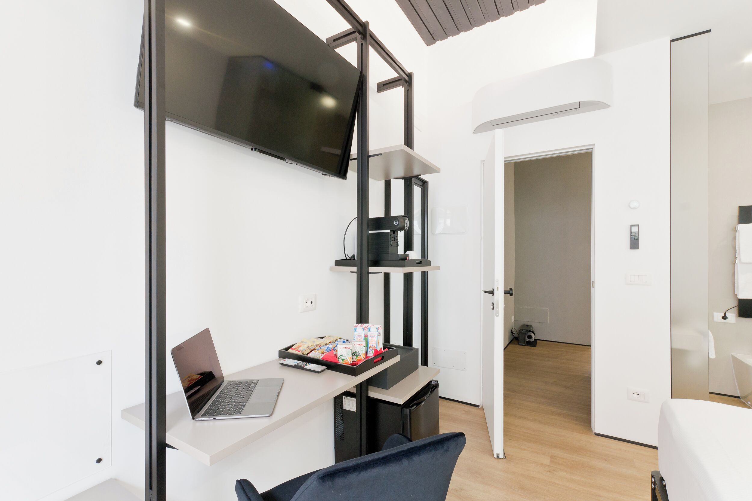 Une chambre d’hôtel moderne équipée d’un téléviseur à écran plat fixé au mur, d’un bureau avec un ordinateur portable, d’une poubelle et d’un petit coin salon.