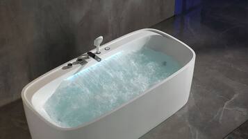 A modern bathtub with a faucet and control knobs, set against a grey tiled floor and wall.