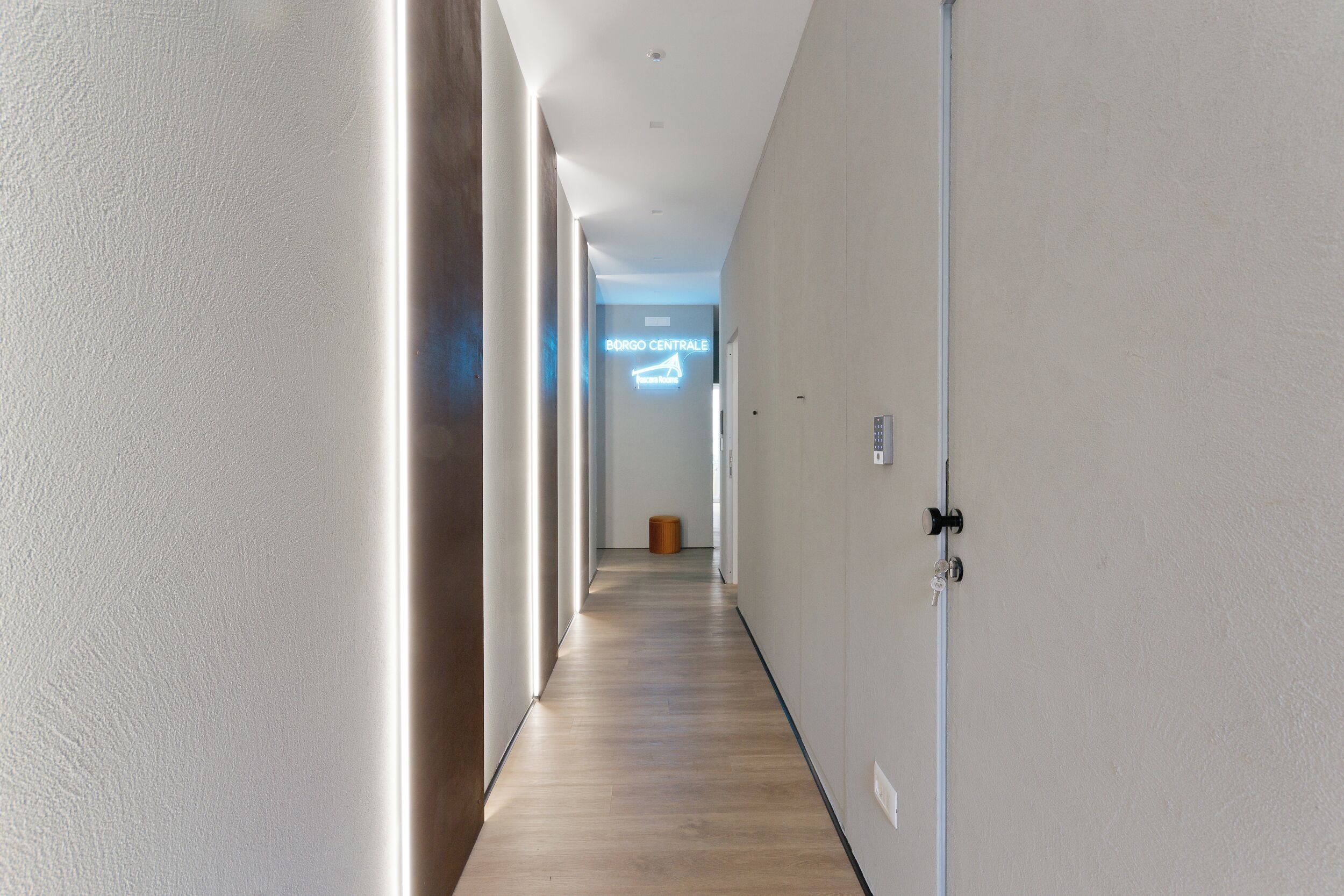 A hallway with a wooden floor, white walls, and a door with a keyhole.