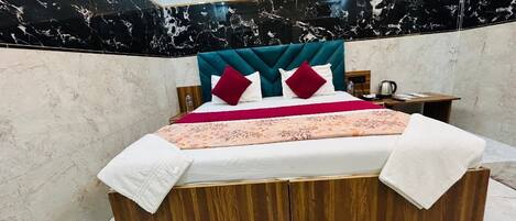 A bed with a wooden frame, a headboard with red and white pillows, and a bedside table with a lamp.
