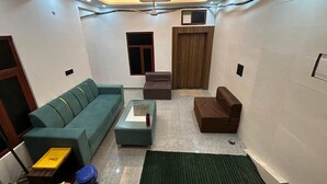 A compact living room with a green sofa, a brown armchair, a small table, and a green rug. - HOTEL JS INN (Ayodhya)
