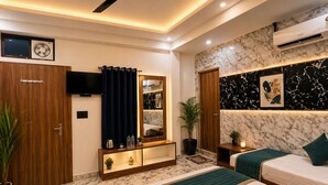 A hotel room with two beds, a ceiling fan, a TV, a mirror, a marble wall, and a potted plant. - HOTEL JS INN (Ayodhya)