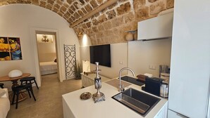 A compact kitchen with a modern sink, a decorative metal rack, and a small dining area with a table and chairs. - Loft Aureo SicilyMyHome (Noto)