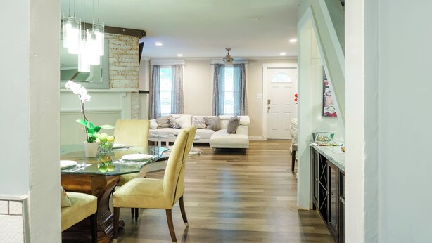 A spacious living area with a sofa, dining table, and chairs. There is a kitchen area with cabinets and a countertop.