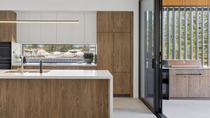 A modern kitchen with a large island, wooden cabinets, and a view of a residential area. - Villa Verda 2 - Luxury Coastal Escape with Private Pool - Holiday Yamba (Yamba)