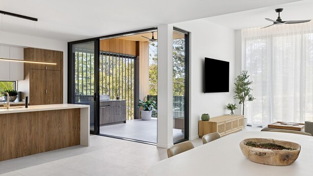 A modern kitchen with a large island, sliding glass doors leading to an outdoor area, a flat-screen TV mounted on the wall, and a ceiling fan. - Villa Verda 2 - Luxury Coastal Escape with Private Pool - Holiday Yamba (Yamba)