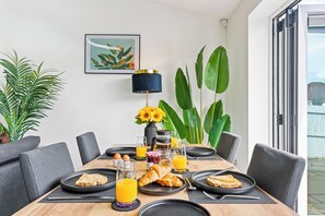 Une table en bois dressée pour le petit-déjeuner, avec des croissants, du jus d’orange et une cafetière.