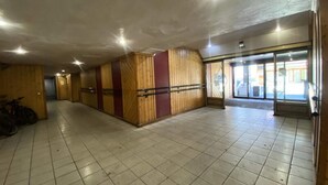 Un couloir aux murs lambrissés et au sol carrelé, qui mène à une porte d’entrée en verre.