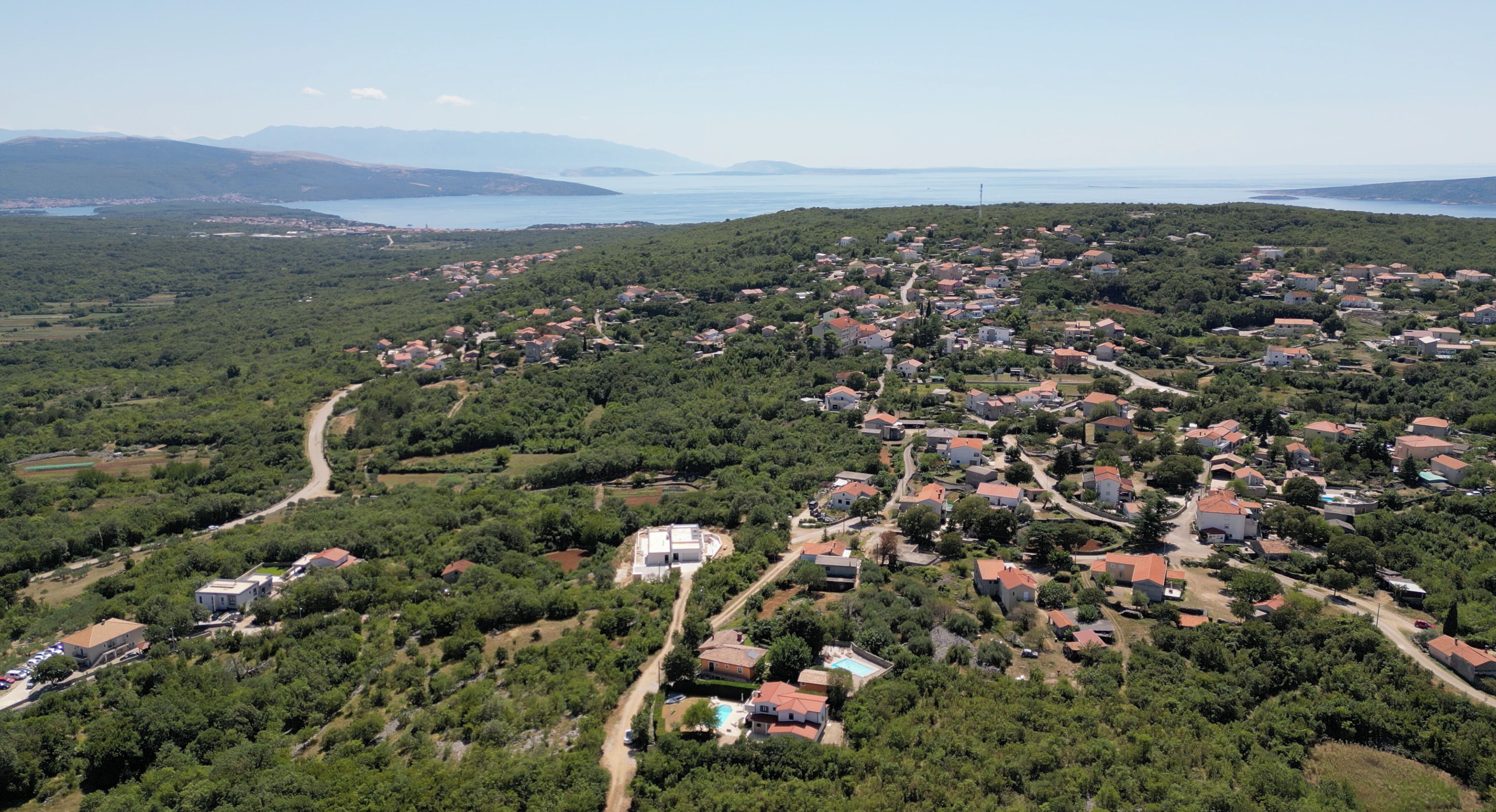 An aerial view of a residential area with houses, roads, and a body of water in the background.