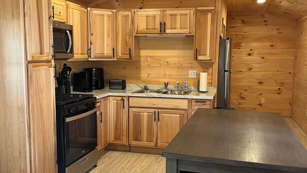 A kitchen with wooden cabinets, a stainless steel refrigerator, a microwave, a stove, and a ceiling fan. - Charming cabin in Brushton NY. Unit 9 (Brushton)